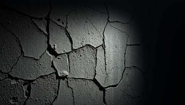Structural fissures in a weathered concrete wall, captured in a moody, high-contrast photograph. The foreground showcases intricate cracks and fractures, with jagged edges and a rugged texture. The middle ground reveals the broader pattern of the fissures, creating a visually striking network of intersecting lines. The background is dimly lit, casting deep shadows that accentuate the depth and dimensionality of the scene. The lighting is dramatic, with soft, directional illumination emphasizing the textural details and creating a sense of depth and atmosphere. The overall mood is one of decay, age, and the relentless forces of nature that gradually erode even the most solid of man-made structures.